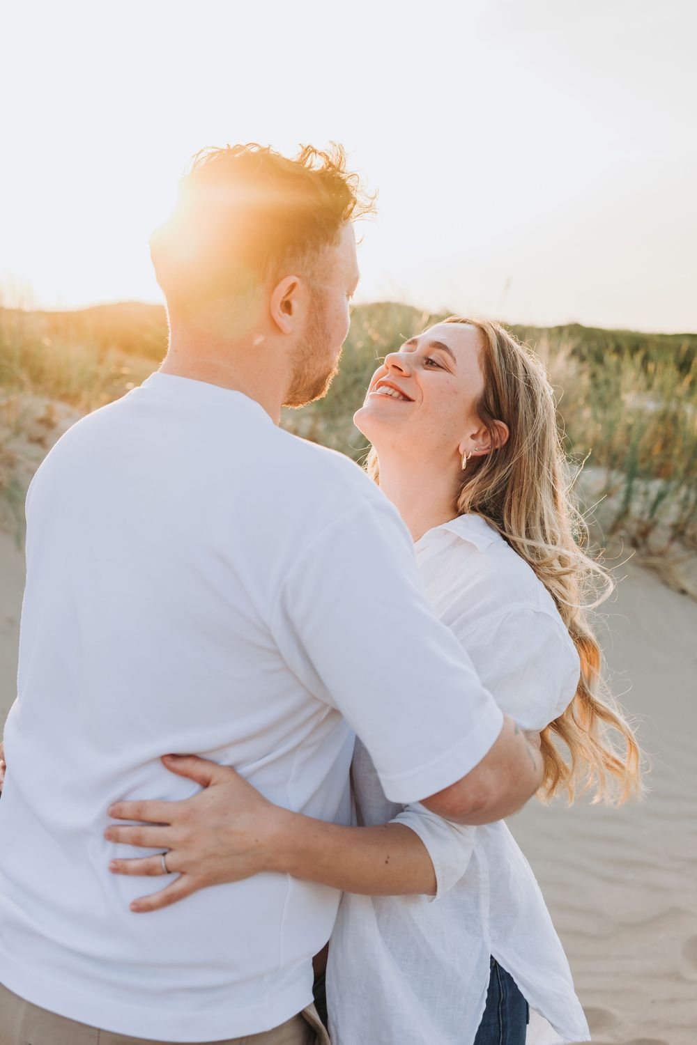 Cinematic warm photo of happy couple embracing on a sunny beach, woman laughing joyfully while man holds her close at golden hour.