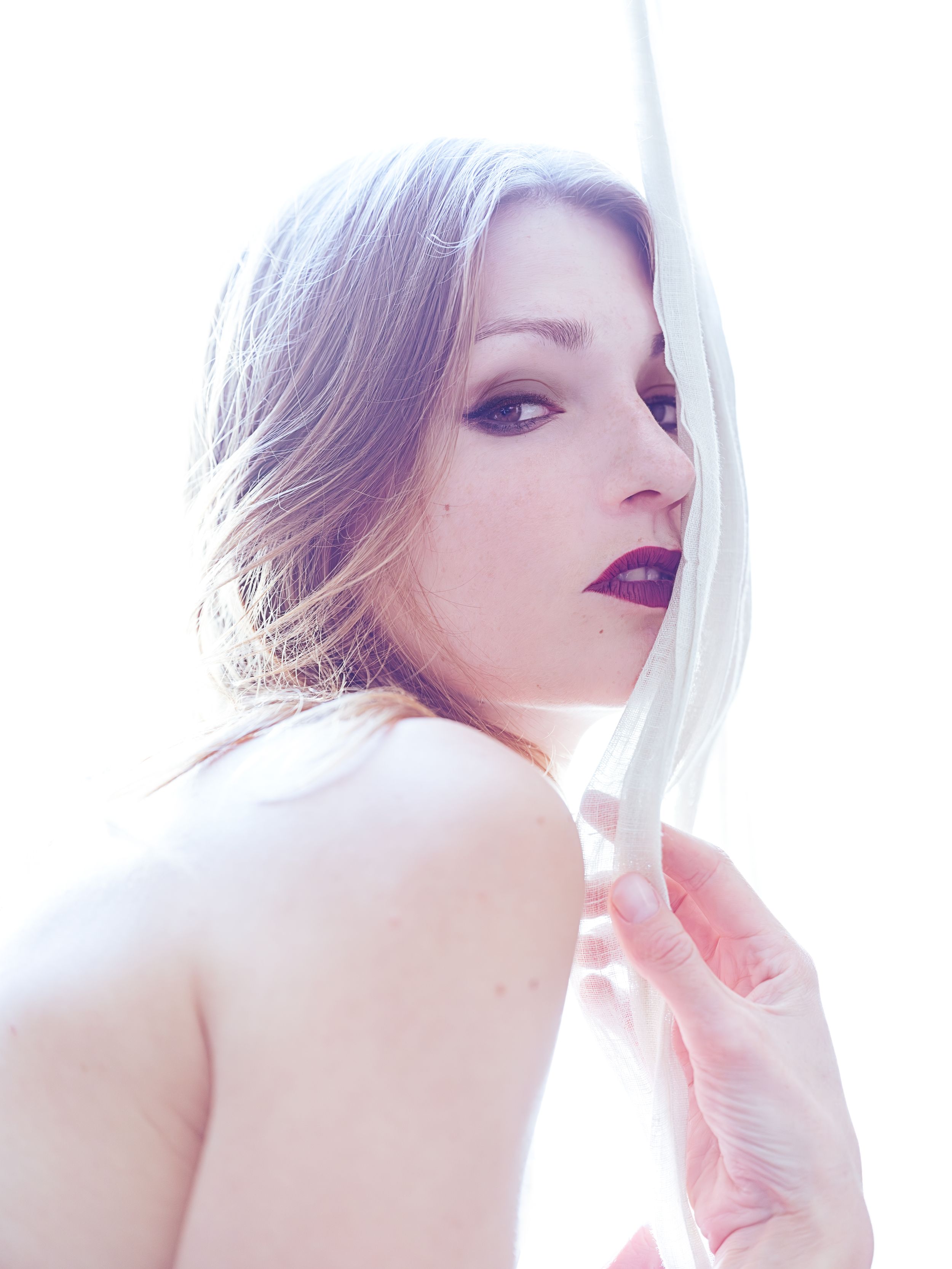 Soft editorial portrait of a model with light-toned hair, hand near her face, bare shoulders