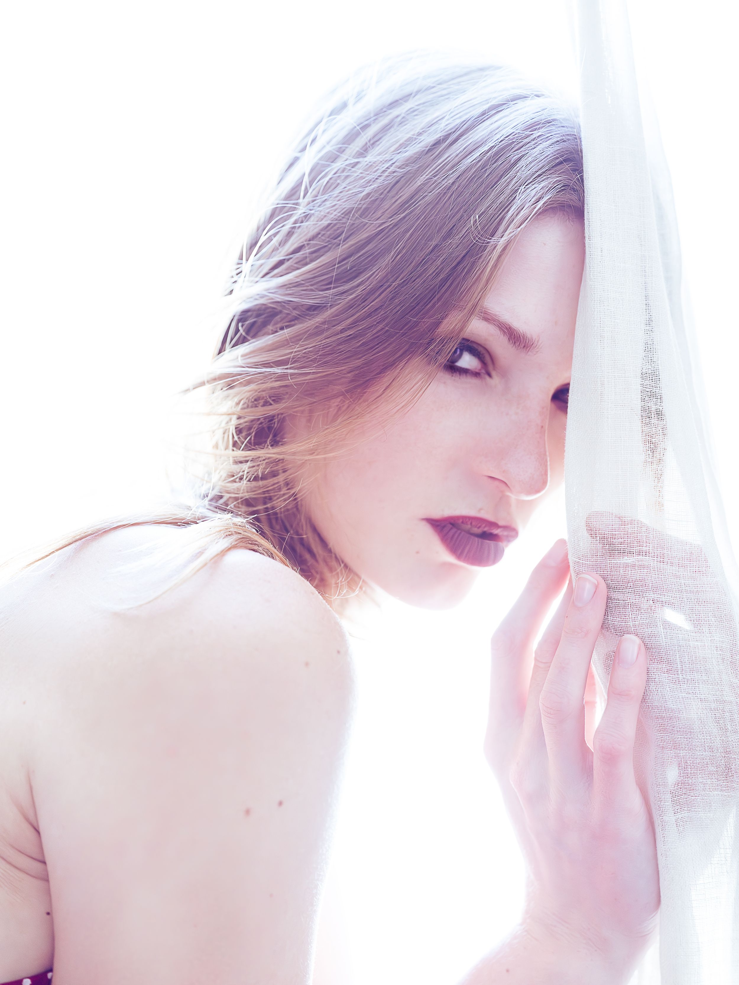 Soft editorial portrait of a model with light-toned hair, hand near her face, bare shoulders