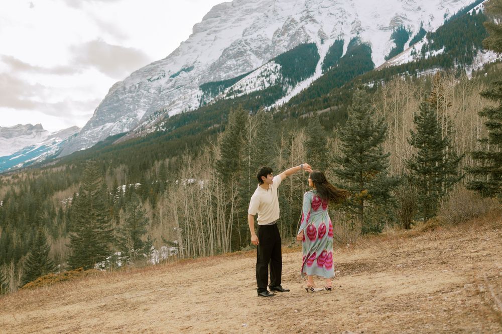 Couple dancing in front of snow-capped mountains and pine trees in Banff, Alberta, Canada.