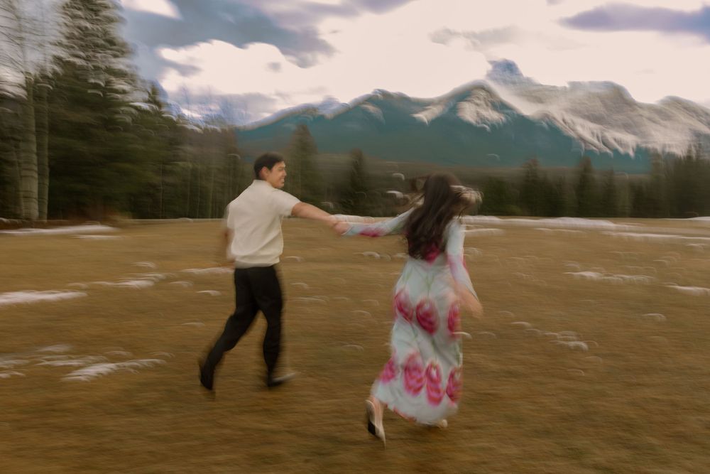 Couple dancing in a mountain meadow with snow-capped peaks and pine trees in the background.