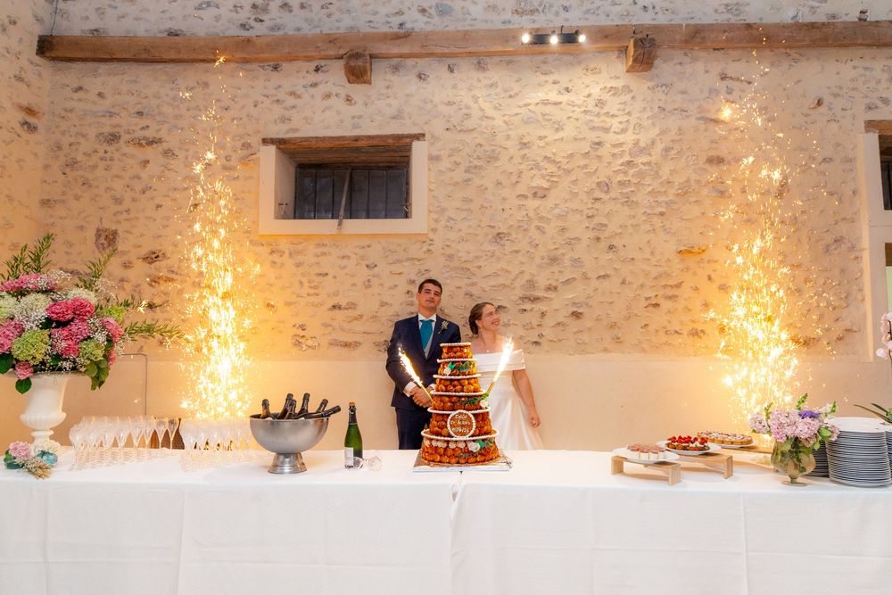 Bride and groom cutting tiered croquembouche wedding cake at elegant stone venue with sparkling light displays.