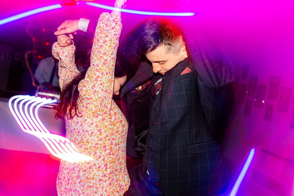 Two people dancing energetically at a nightclub with vibrant neon pink and purple lights in the background.