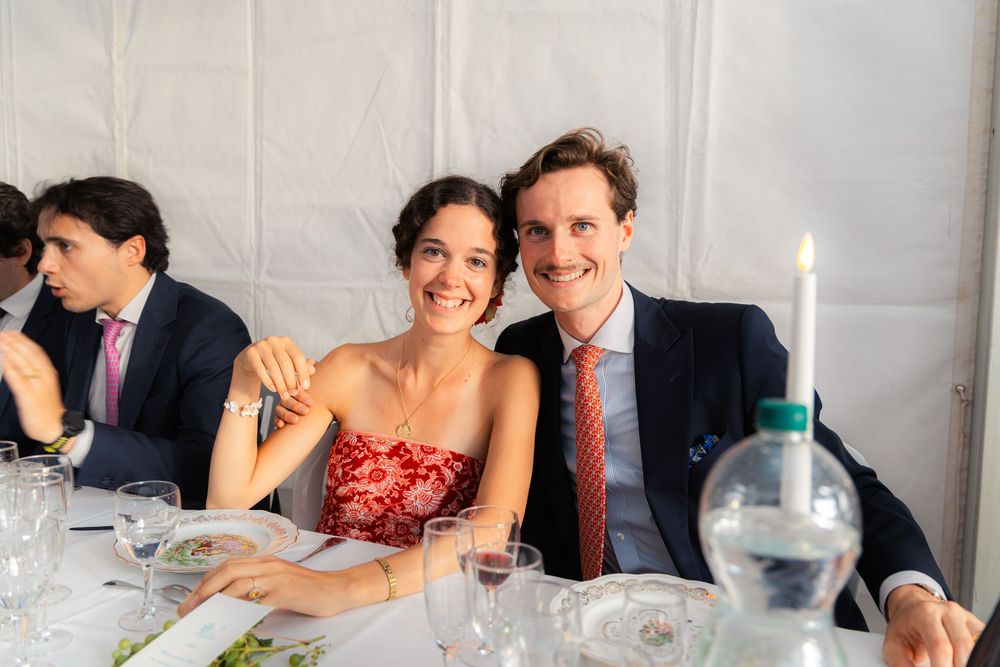 Smiling couple posing together at an elegant outdoor wedding reception dinner table with candles and glassware.