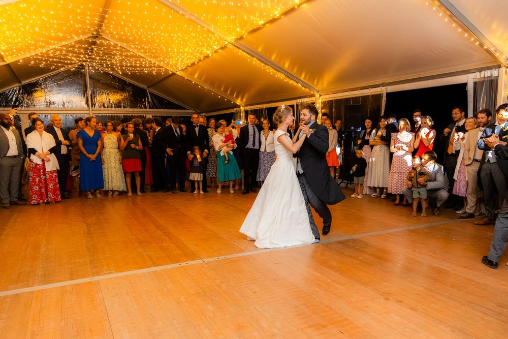 Bride and groom share their first dance on a wooden floor under warm fairy lights at an elegant wedding reception.
