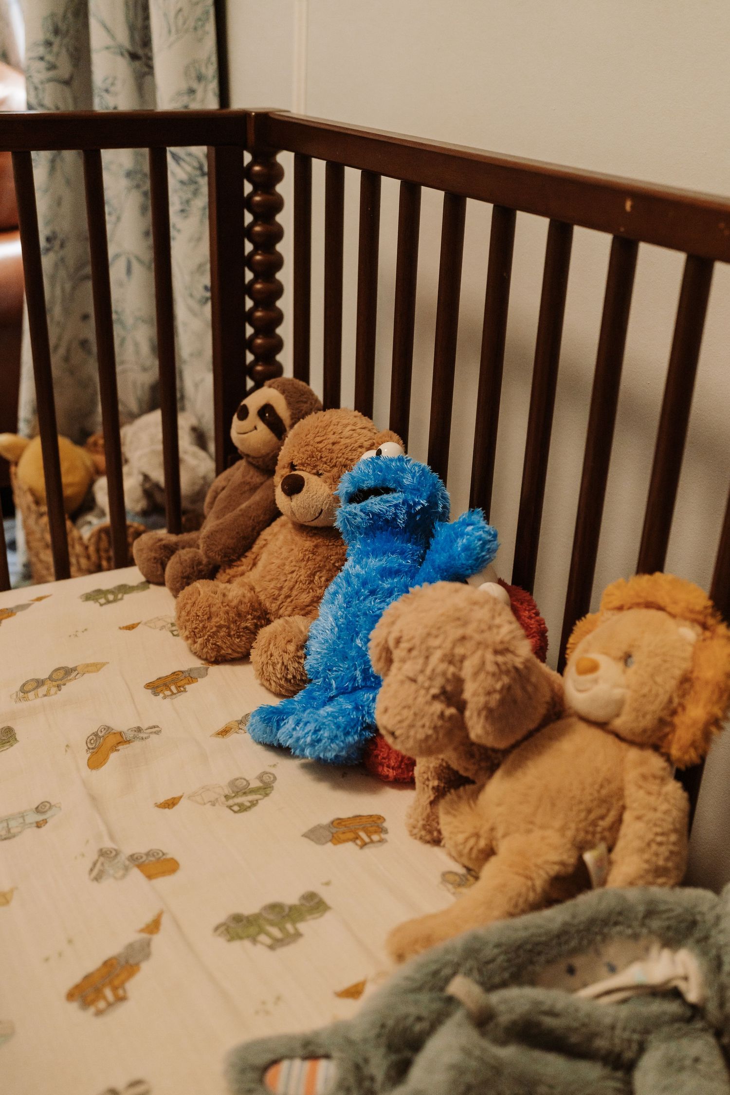 Stuffed animals including Cookie Monster and teddy bears arranged in a wooden baby crib with animal print bedding.