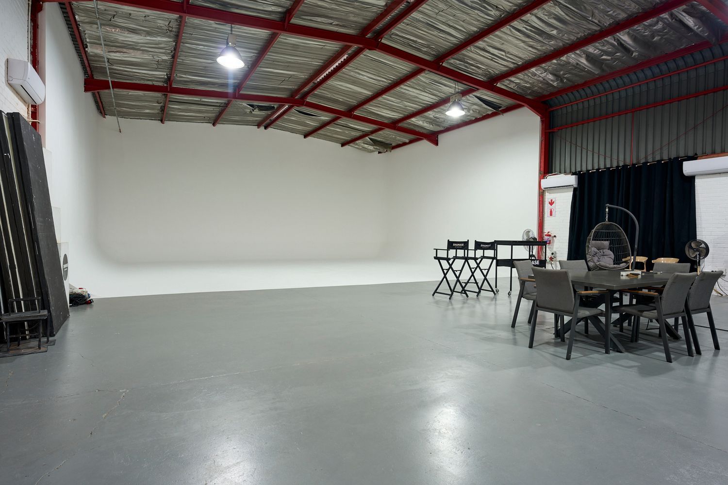 Spacious industrial photography studio with white backdrop, concrete floors, and furniture props at Shamase Studios.