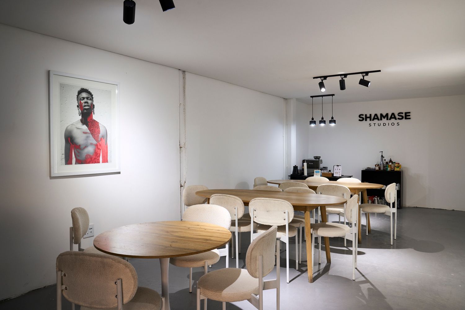 Modern studio lounge area with round wooden tables, minimalist chairs, and portrait artwork at Shamase Studios.