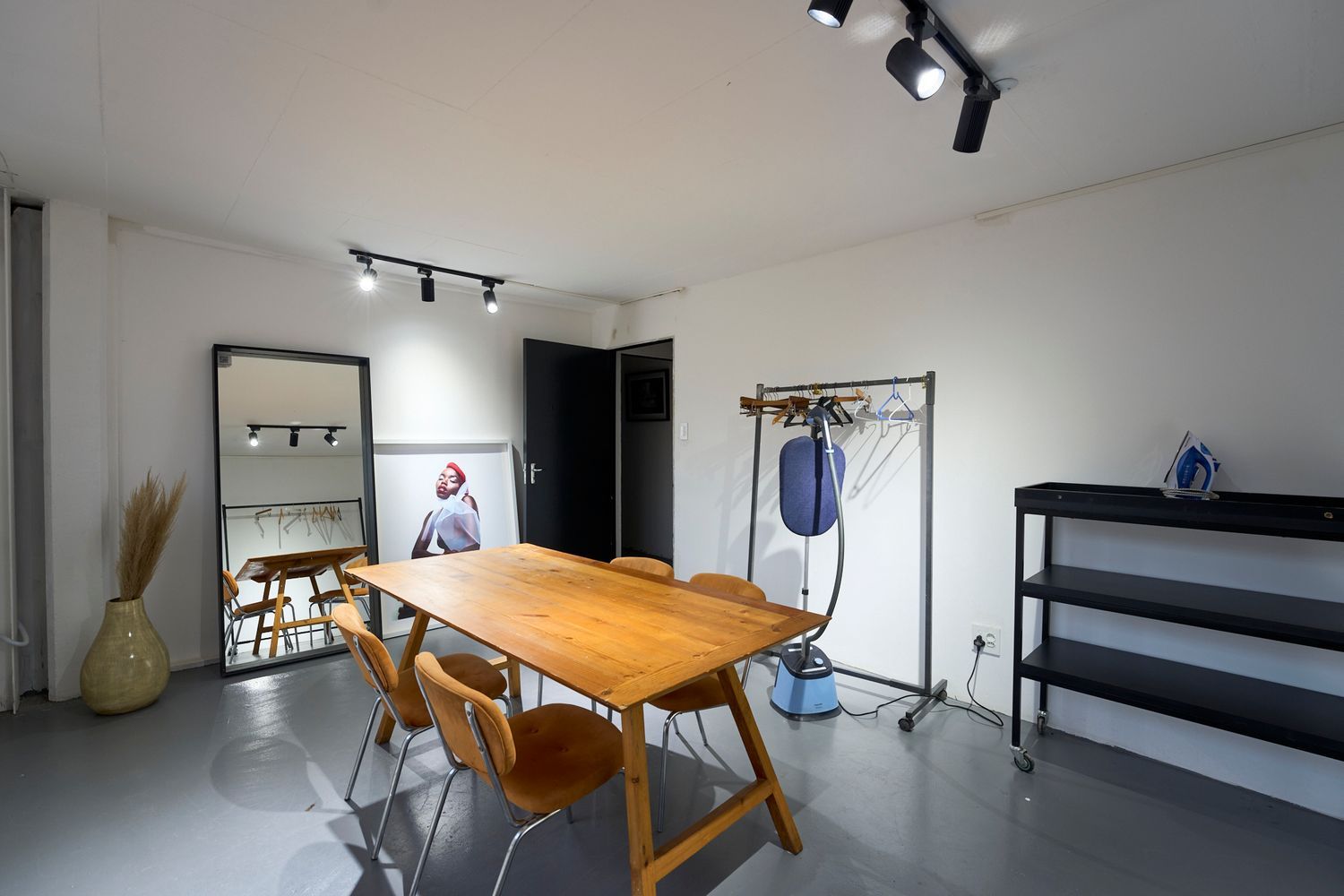 Professional studio styling room with wooden table, clothing rack, shelving unit, and track lighting.