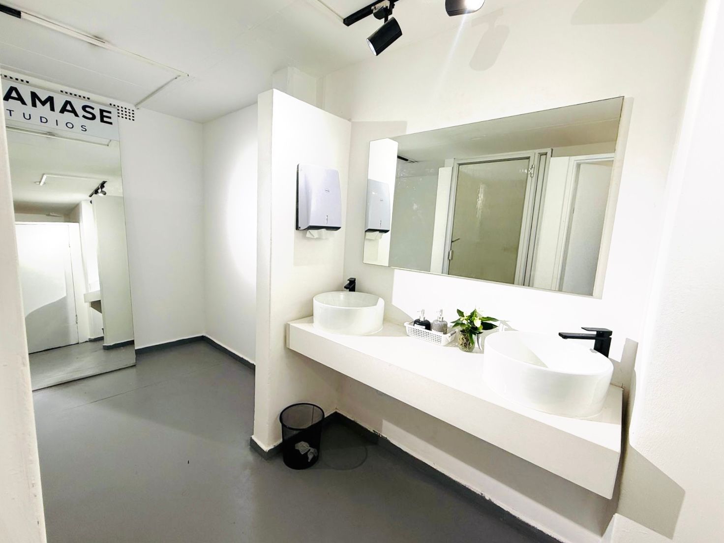 Clean modern studio bathroom with double vessel sinks, large mirror, and white walls at Shamase Studios.
