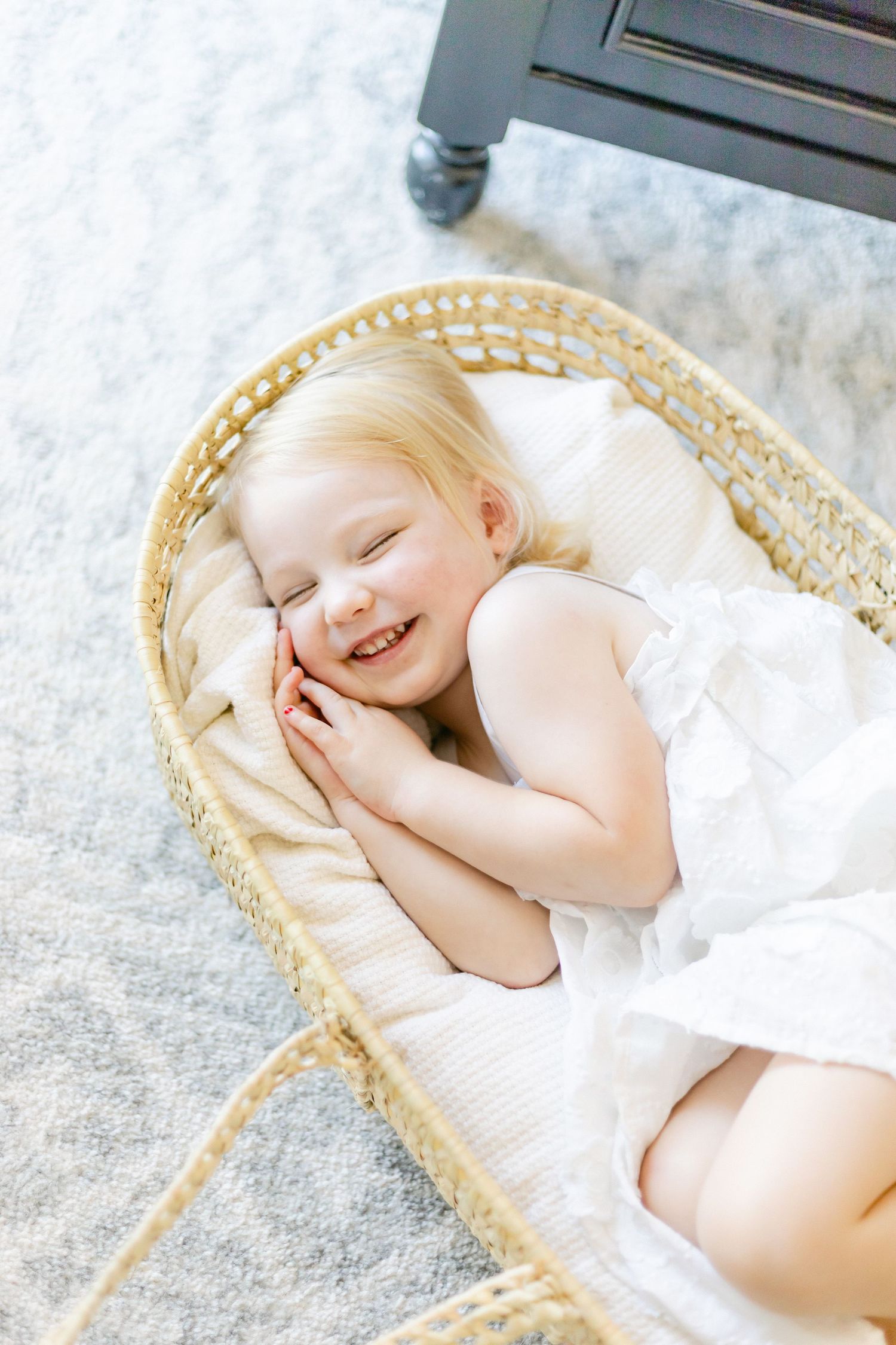 Mother sitting in a gray nursery glider chair, cradling her newborn baby, surrounded by a white crib and dresser.