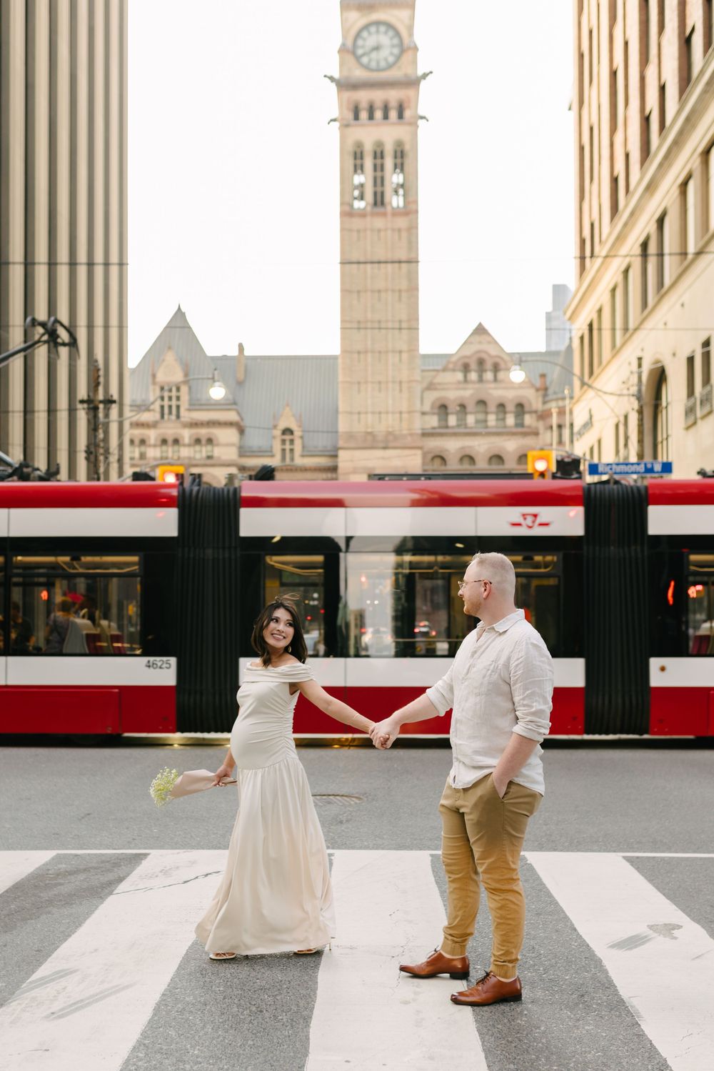 Expectant couple dancing on a Toronto crosswalk in front of a streetcar.