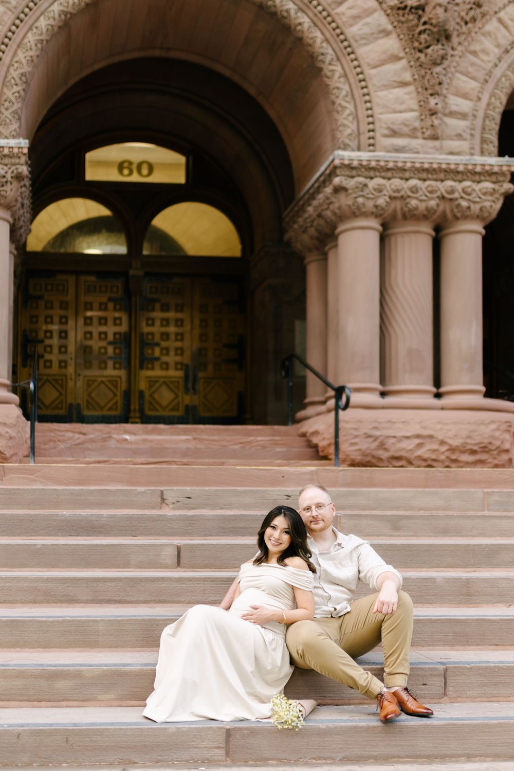 Expectant couple sitting together on the steps of a stone entrance.