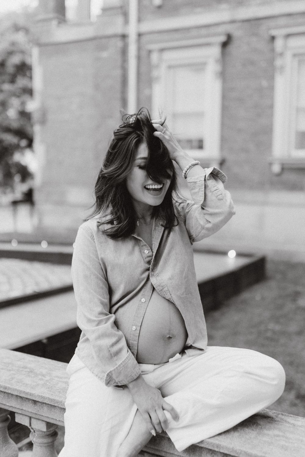 Expectant mother seated outside a brick building, black and white.