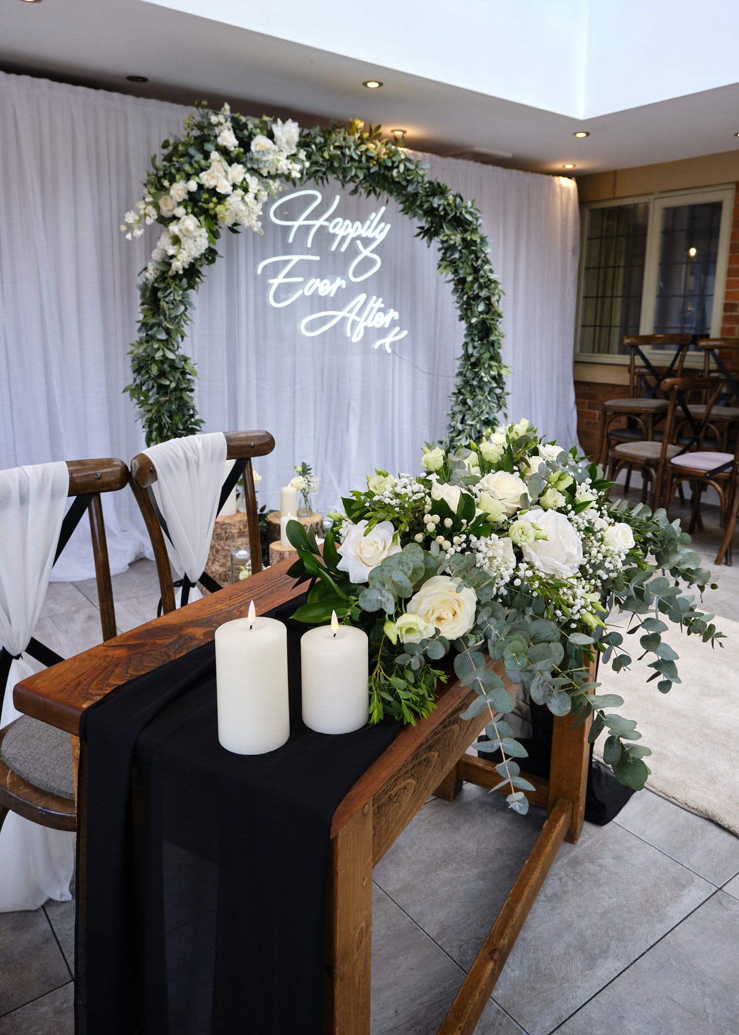 Elegant wedding sweetheart table with white floral arch, Happily Ever After neon sign, candles, and greenery decor.
