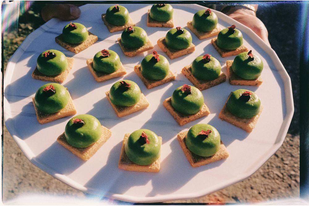 A white plate of green matcha mousse appetizers on crackers, topped with red berry garnishes, served at an outdoor event.