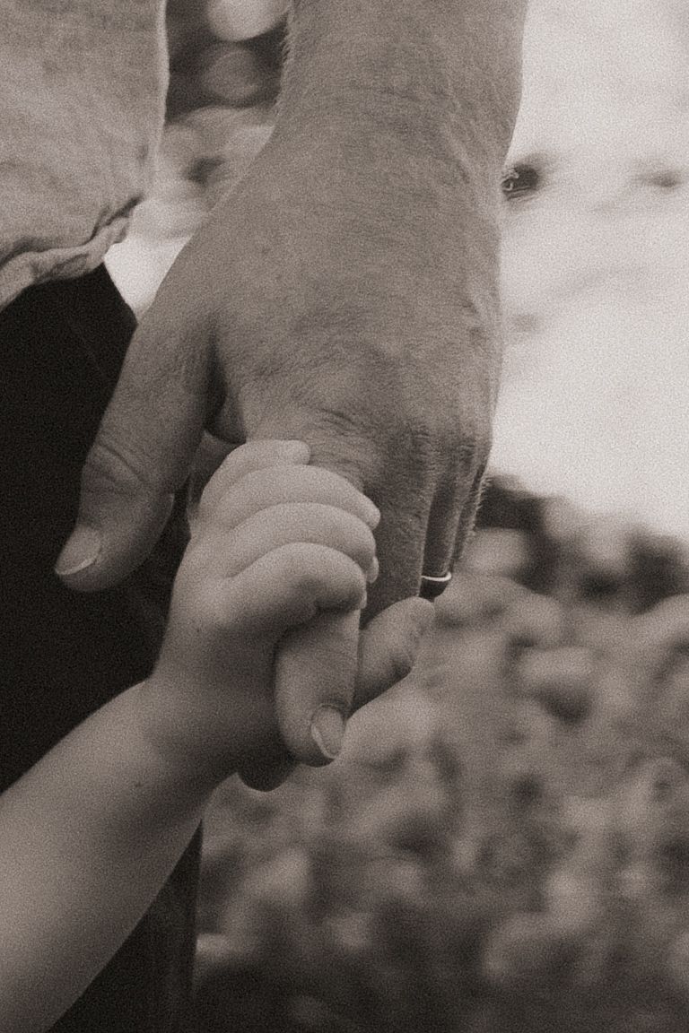 Black and white photo of an adult and small child holding hands, symbolizing family bond and parental love.