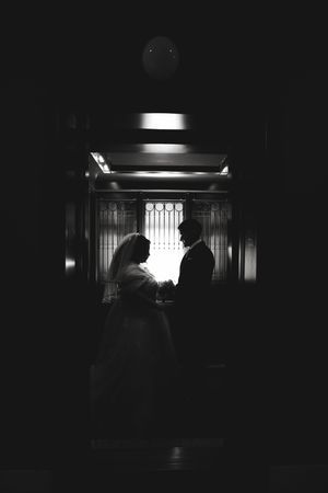 Black and white silhouette of bride and groom facing each other in dimly lit doorway on wedding day.