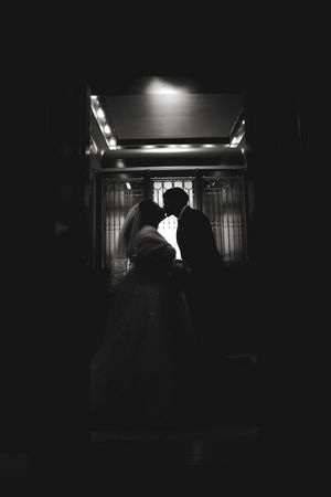 Black and white silhouette of a bride and groom sharing a romantic moment in a dimly lit elegant doorway.