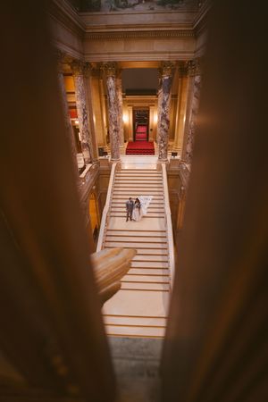 Aerial view of bride and groom on grand staircase with red carpet in elegant historic building.