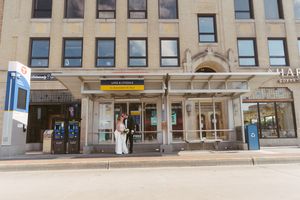 Couple in wedding attire posing outside a city building entrance on a sunny day.