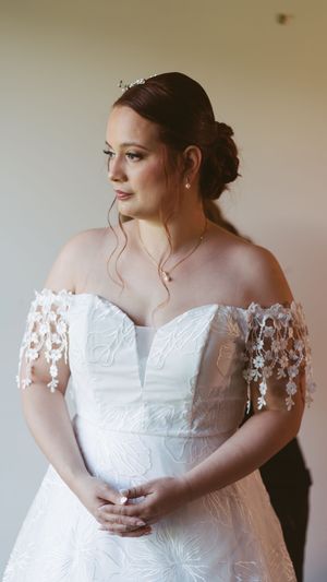 Elegant bride in off-shoulder lace wedding gown with floral appliques and updo hairstyle adorned with a tiara.