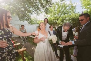 Bride and groom sign wedding documents outdoors surrounded by smiling guests in sunny garden.