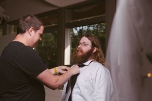 Man helping another man with a tie while getting dressed for a formal event.
