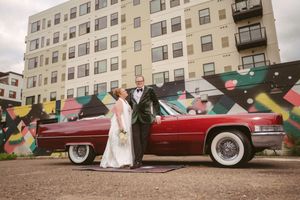 Bride and groom posing beside a classic red Cadillac convertible in front of a colorful street mural.