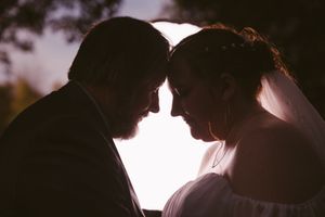 Romantic silhouette of bride and groom touching foreheads at sunset during outdoor wedding ceremony.