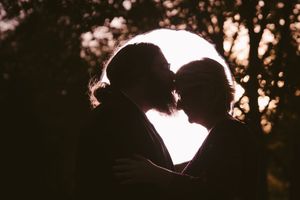 Romantic silhouette of a couple kissing against a glowing sunset backdrop with trees in the background.