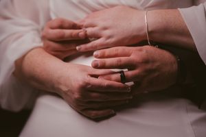 Close-up of couple's hands intertwined showing wedding rings and bracelet on wedding day.