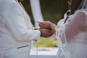 Bride and groom exchanging rings during an outdoor wedding ceremony, dressed in white lace gown and ivory suit.