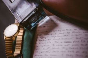 Vintage gold wristwatch beside an ink pen and handwritten letter on paper, nostalgic flat lay composition.