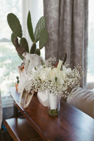 White roses and baby's breath bouquet in vase beside decorative skull and cactus.