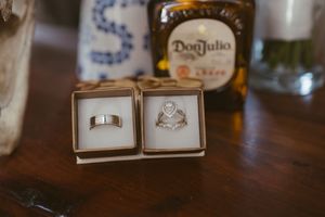 Two wedding rings in open boxes beside a Don Julio tequila bottle on a wooden table.
