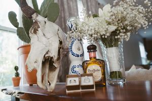 Rustic wedding decor with cow skull, Don Julio tequila, salt shakers, and white floral arrangement on wooden table.