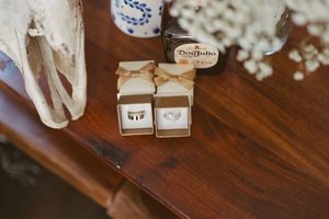 Two wedding rings displayed in rustic kraft paper boxes with twine bows on a wooden table.