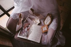 Bridal accessories flatlay featuring lace heels, wedding rings, necklace, and open journal on chair.