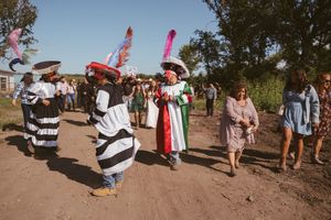 Traditional Mexican dancers in colorful costumes parade down a dirt road during a festive outdoor celebration.