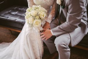 Close-up of bride and groom holding hands with a white rose bouquet on wedding day.