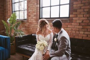 Bride and groom sharing an intimate moment on a leather sofa in a rustic brick wedding venue.