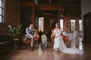 Bride and groom seated in leather chairs in a stylish industrial brick wedding venue.