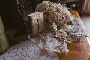 Elegant wedding flat lay with blush roses bouquet, ornate jewelry, lace details, and decorative book on wooden table.