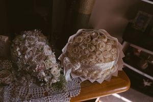 Two elegant white rose bouquets resting on a wooden table with lace cloth in soft vintage lighting.