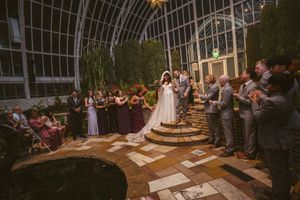 Wedding party celebrates with bride and groom in stunning botanical garden venue with lush greenery.