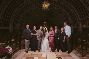 Wedding party poses under ornate iron archway with star pendant light, bride in white gown holding bouquet.