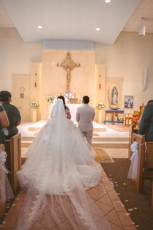 Bride and groom kneeling at church altar during Catholic wedding ceremony with crucifix.