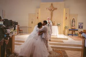 Bride and groom sharing first kiss at Catholic church altar during wedding ceremony.