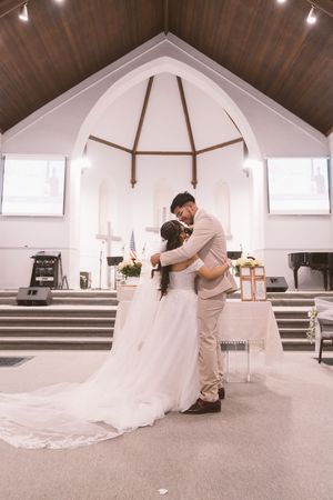 Bride and groom share an intimate embrace at the altar of a white church during their wedding ceremony.